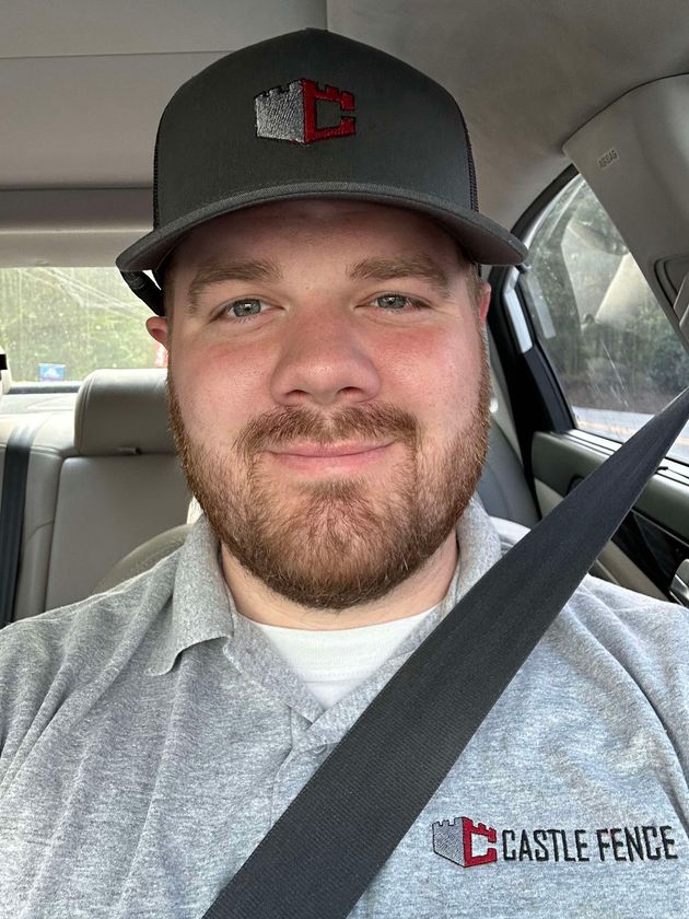 A man with a beard is sitting in a car wearing a hat and a seat belt.