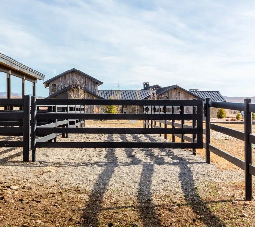 A black fence is surrounding a dirt field with a house in the background.