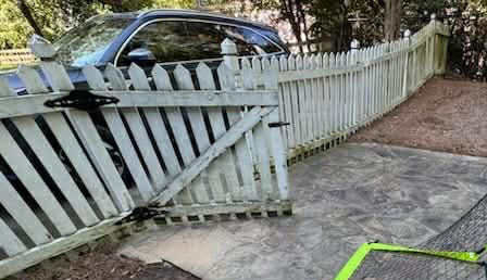 White picket fence with a broken gate; a car is visible behind the fence.