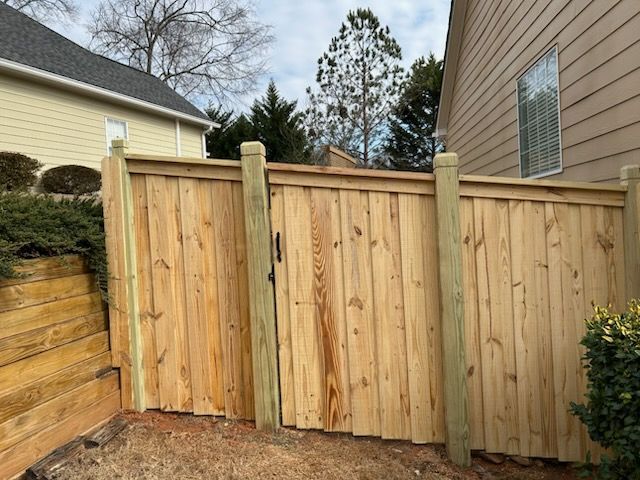 Wooden fence and gate separating two houses, with a retaining wall on the left.