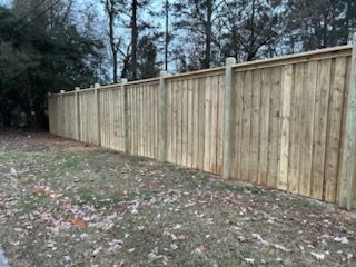 Wooden privacy fence in a grassy area with trees in the background.
