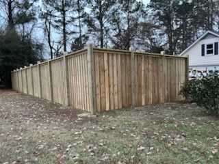 Wooden privacy fence surrounding a grassy yard with a house in the background.