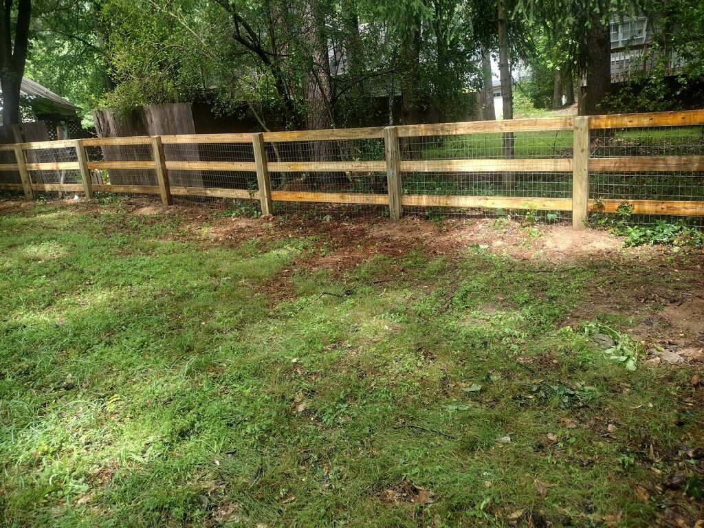 A wooden fence surrounds a lush green field.