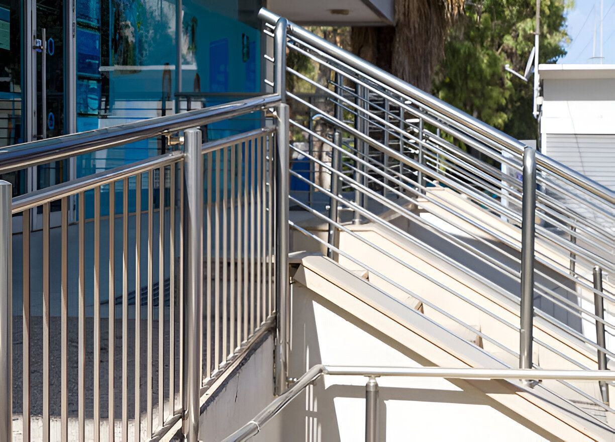 A stainless steel railing surrounds a set of stairs leading up to a building.