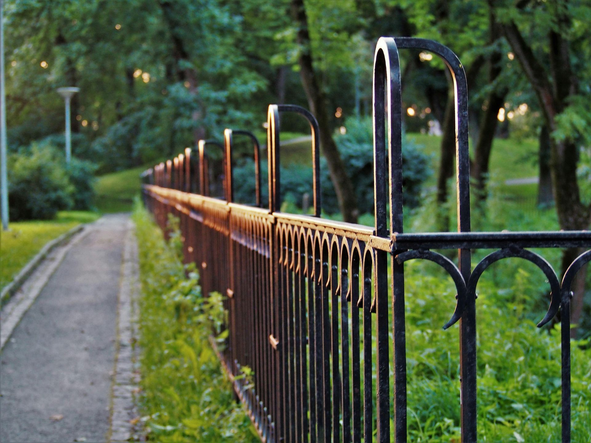 A wrought iron fence surrounds a path in a park.