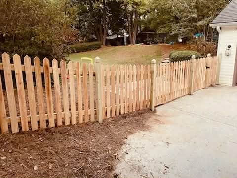 Wooden picket fence in a yard, extending from a concrete driveway into a grassy area.