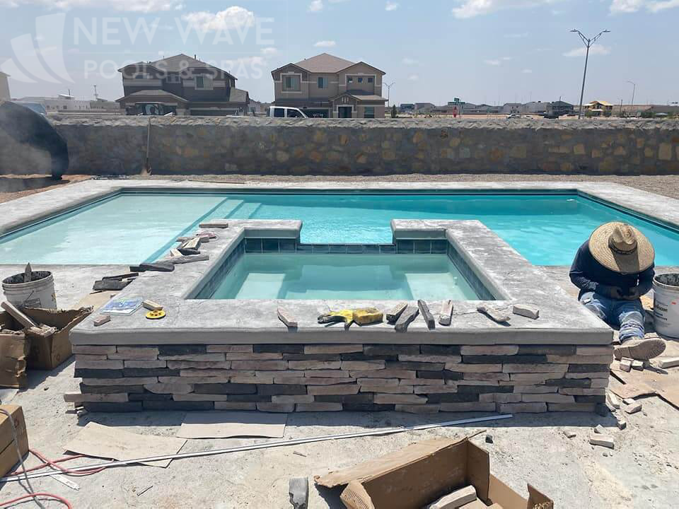 A man is working on a hot tub next to a swimming pool.