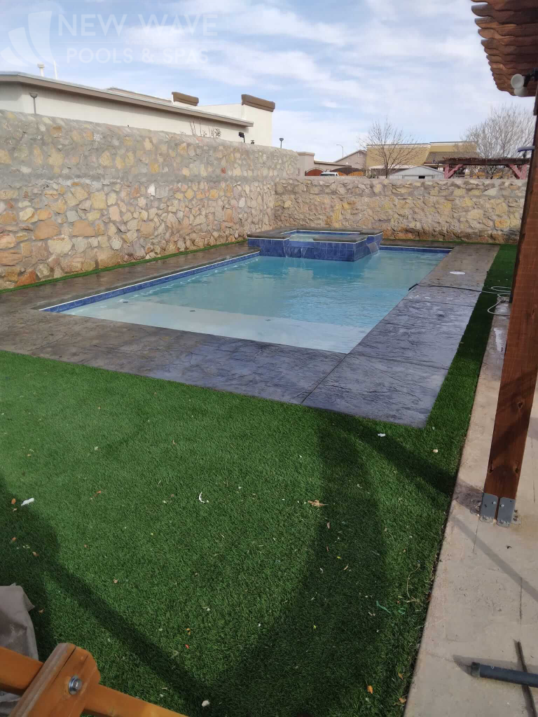 A large swimming pool is surrounded by a stone wall and a lush green lawn.