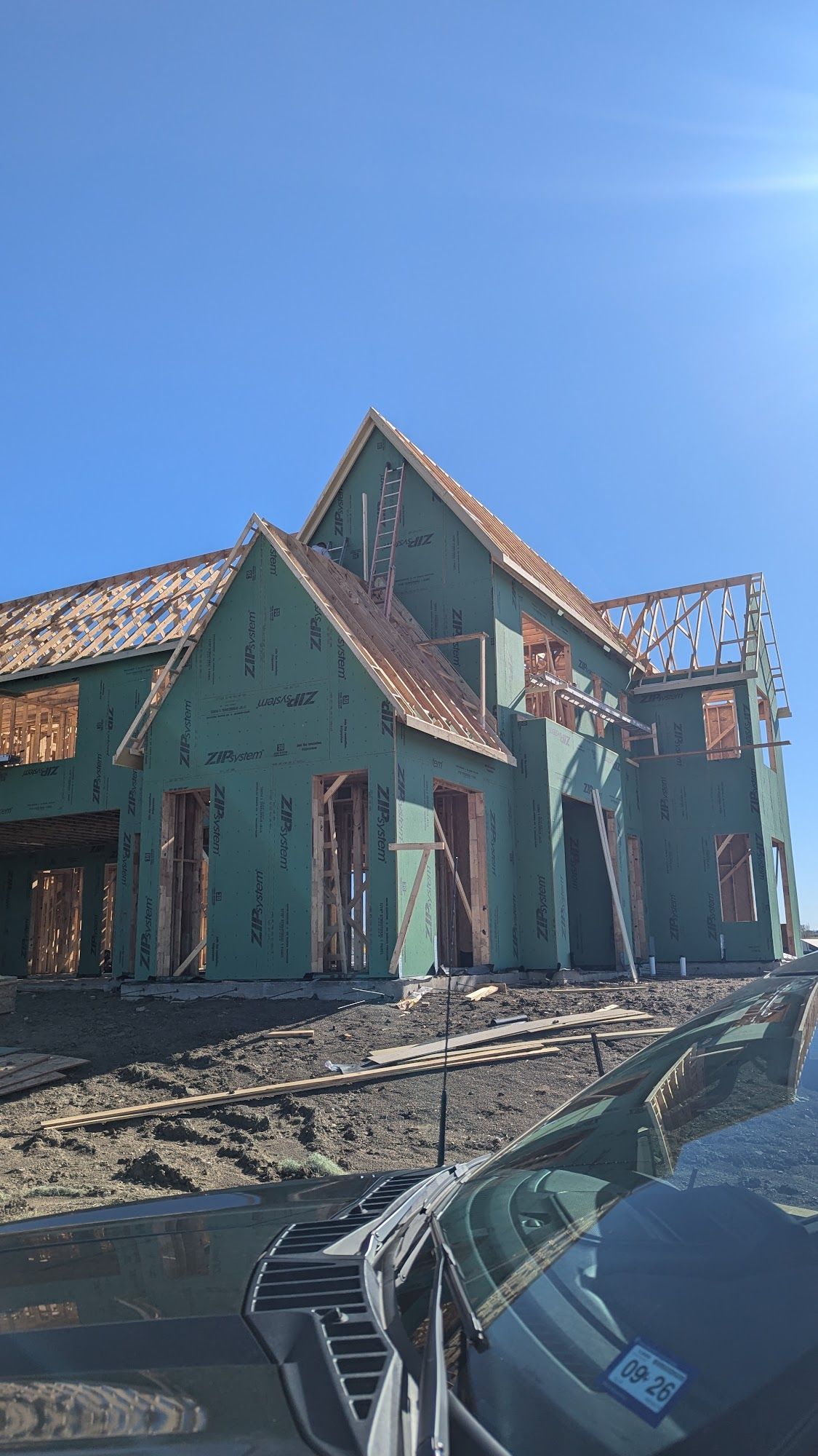 House under construction with green siding, exposed framing, and blue sky.
