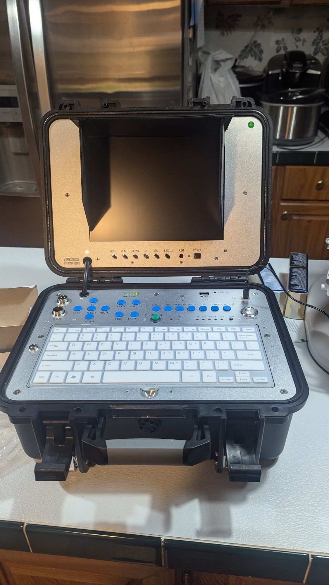 Black case with integrated keyboard and screen. Control buttons along top, and an external remote.