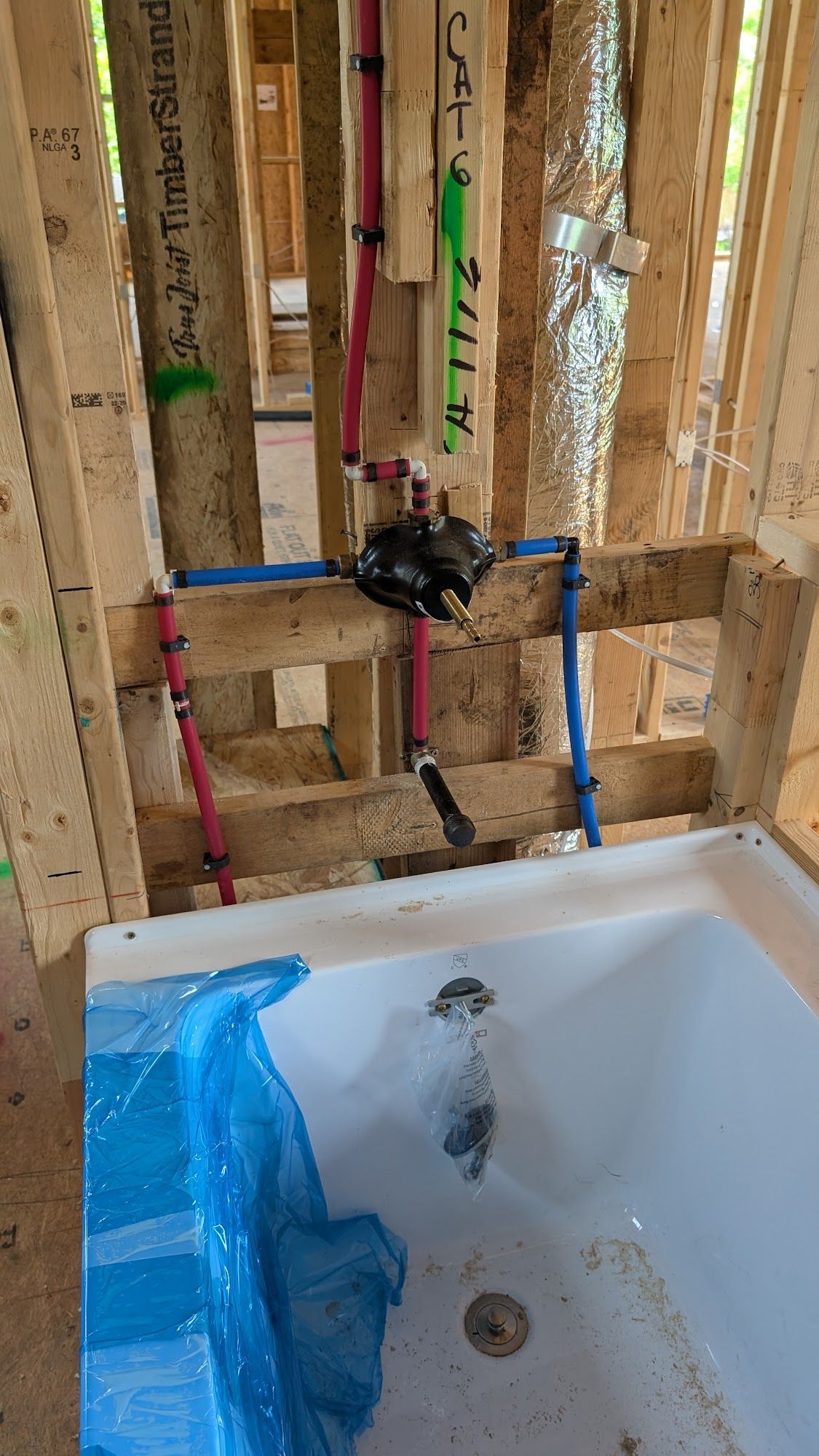 Plumbing rough-in for a bathtub: red and blue pipes connected to a valve inside a partially constructed wall.