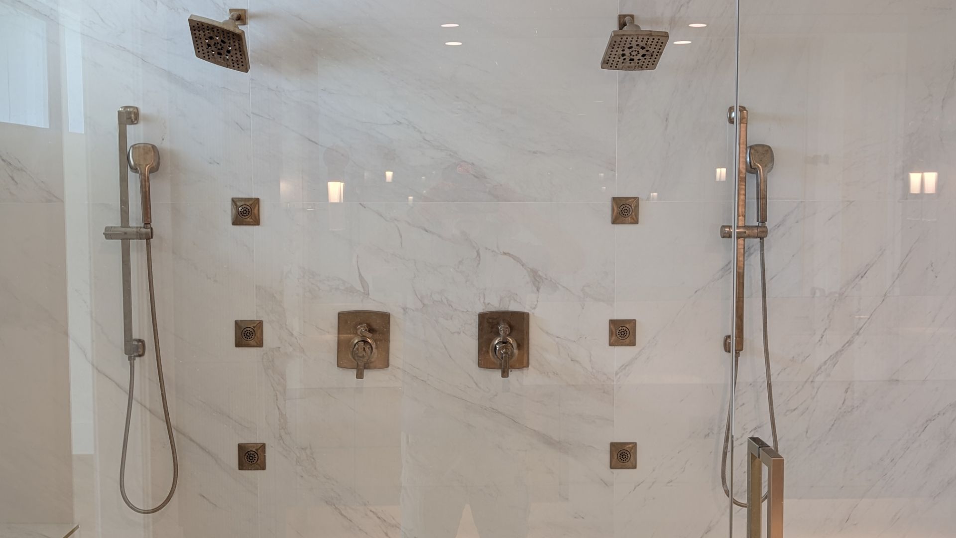 Modern double shower with bronze fixtures and marble-look tile behind glass doors.