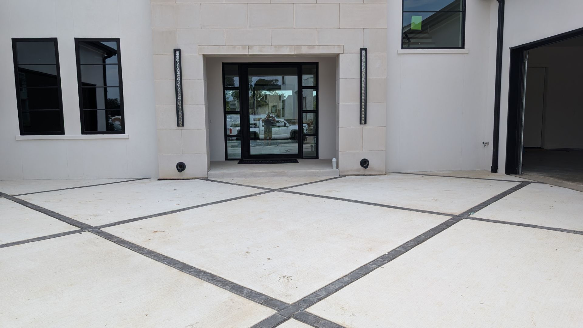 Exterior view of modern white house with glass front door, black trim and decorative pavement.