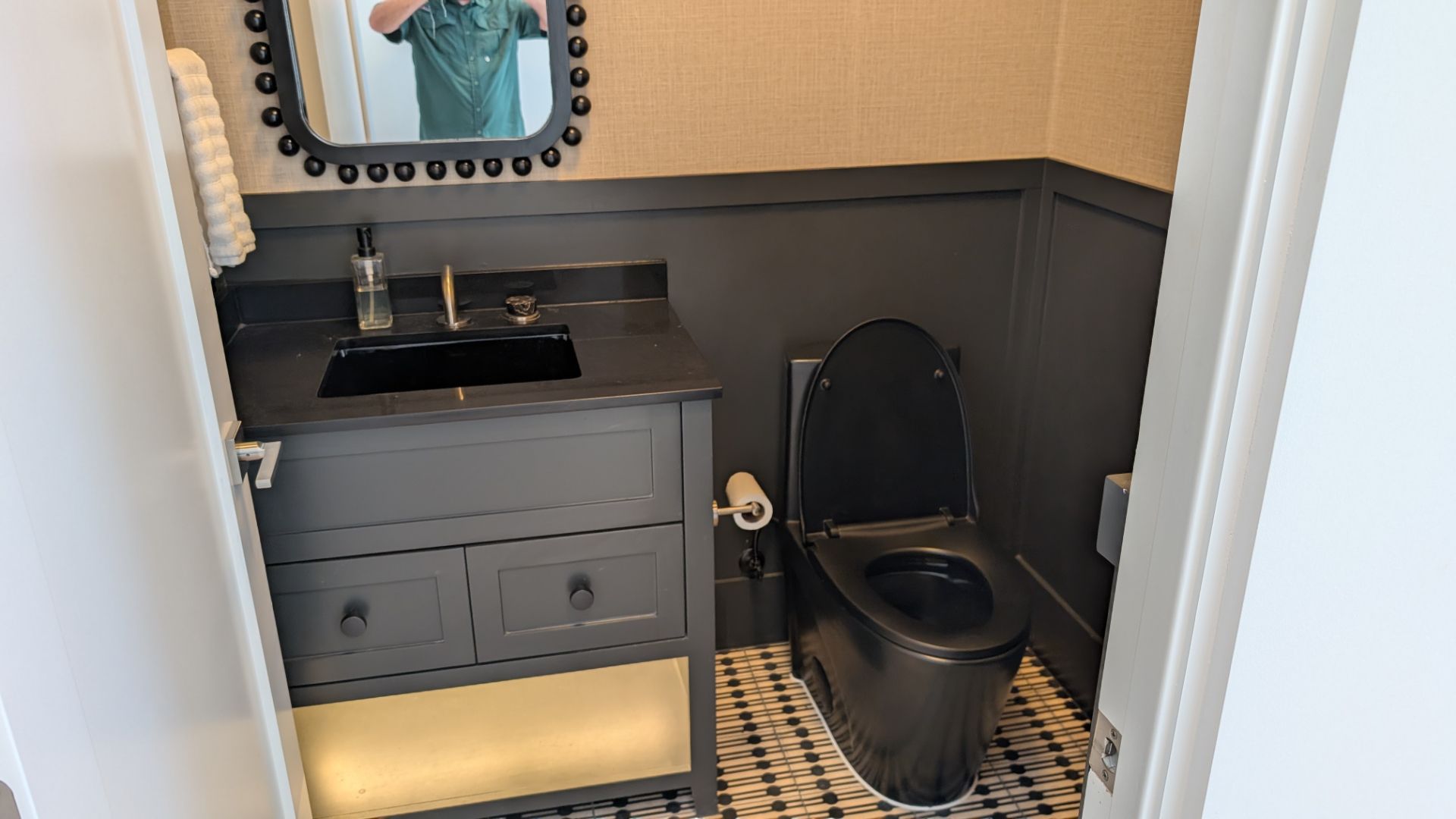 Dark-themed powder room with black toilet, vanity, and trim, plus a patterned tile floor.