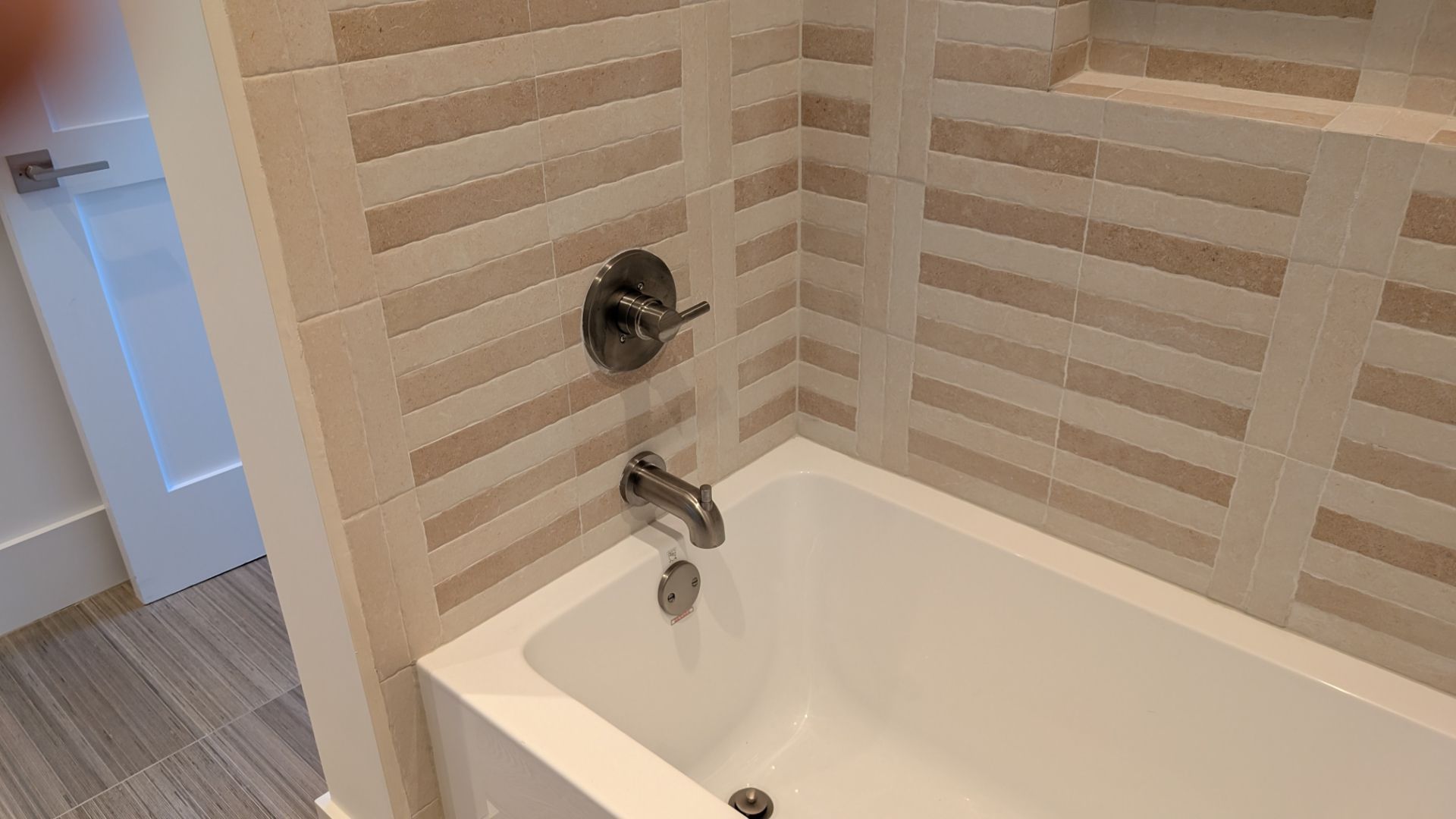 Bathtub with chrome fixtures, tan and white horizontal tile, and a built-in shelf.