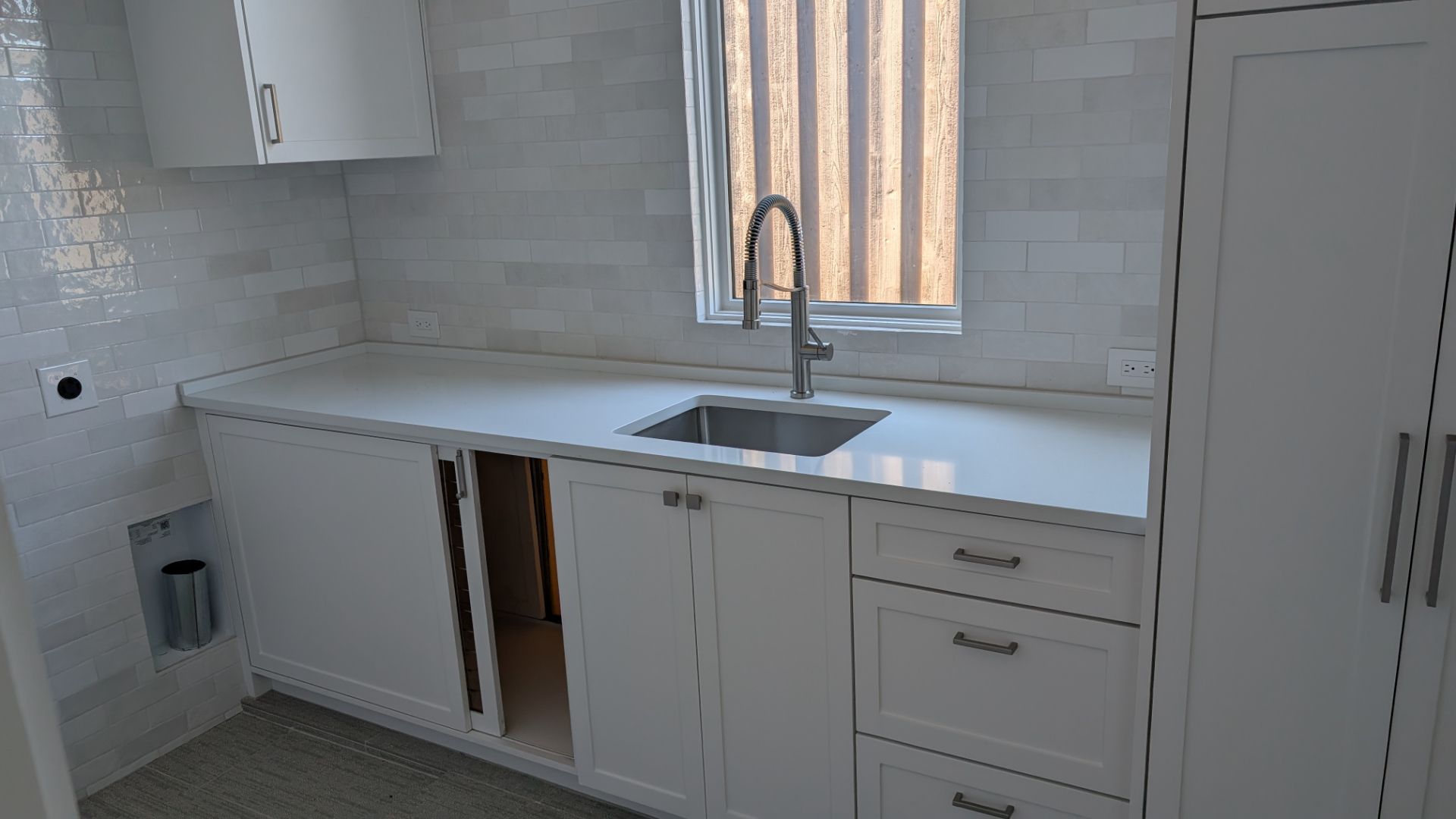 White kitchen cabinets with a white countertop and silver faucet in front of a window.