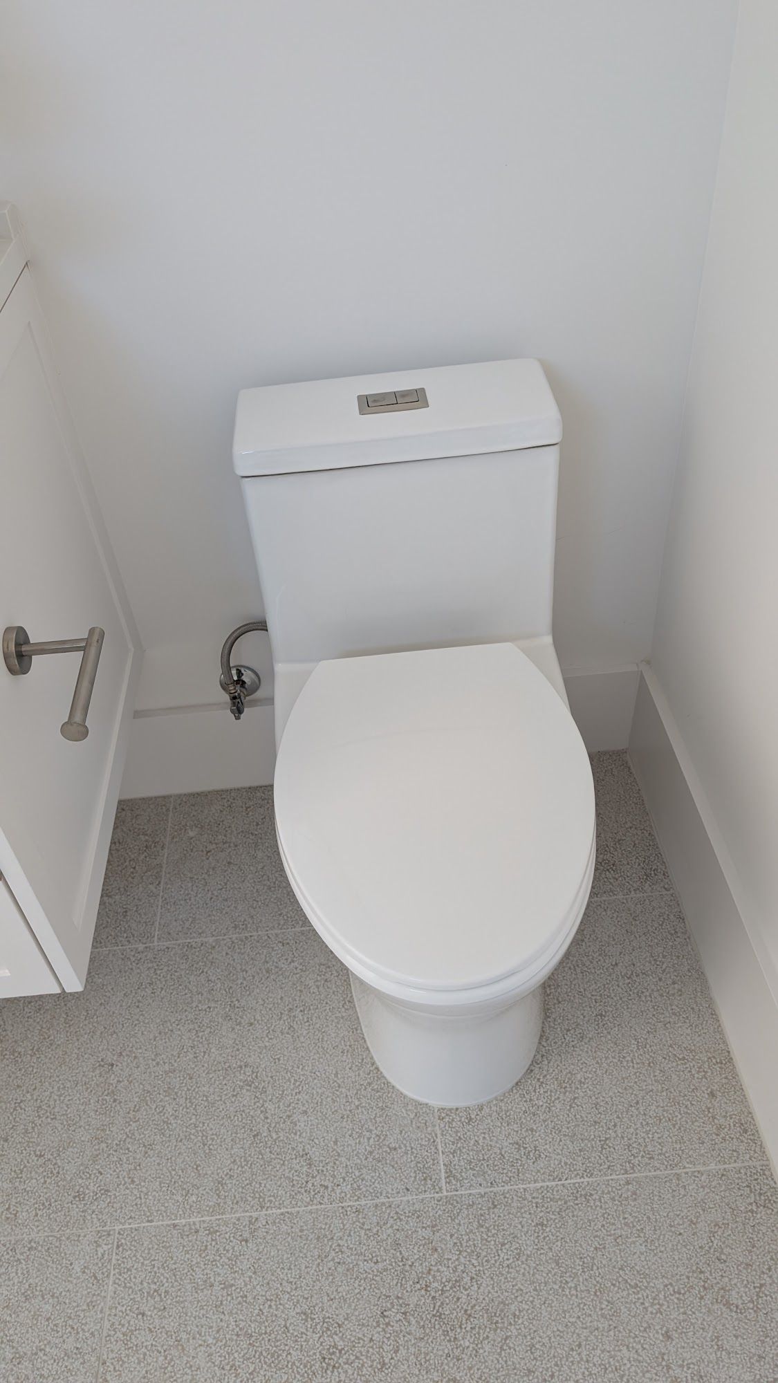 White toilet in a small bathroom with white walls and speckled gray flooring.