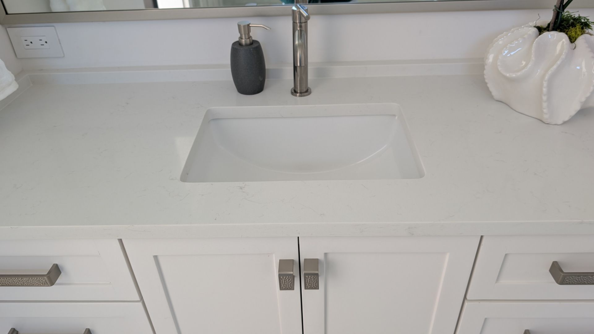 White bathroom vanity with a rectangular sink, soap dispenser, and decorative vase.