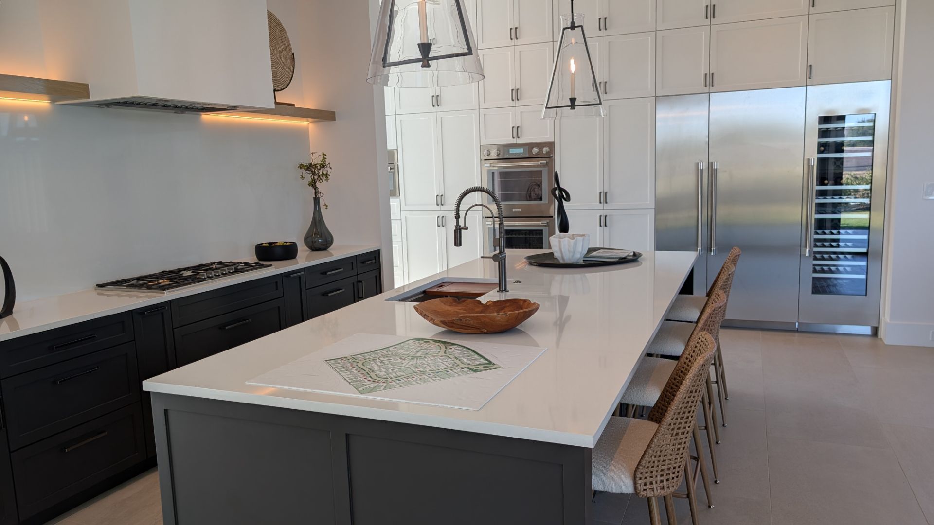 Modern kitchen with white countertops, dark gray island, stainless steel appliances, and wood chairs.