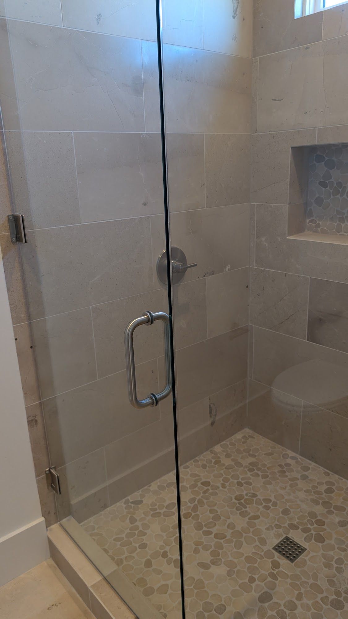 Glass shower with pebble floor and stone tile walls.