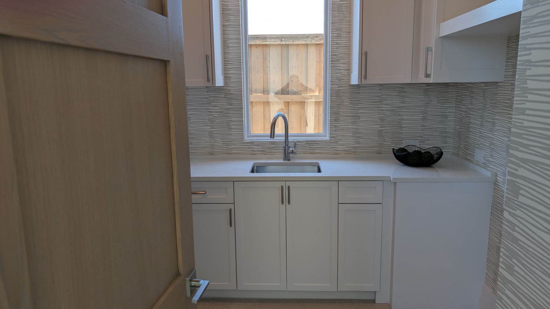 White cabinetry with a sink, window, and patterned backsplash in a small utility room.
