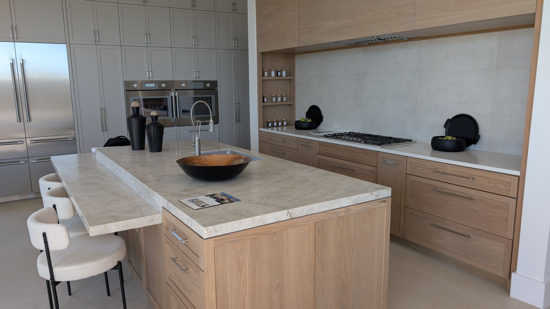 Modern kitchen with light wood cabinets, stone countertops, and a large island with seating.