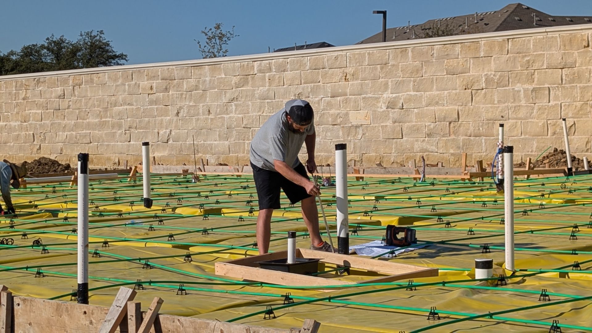 Construction worker installing poles on a prepared ground covered with yellow and green materials.