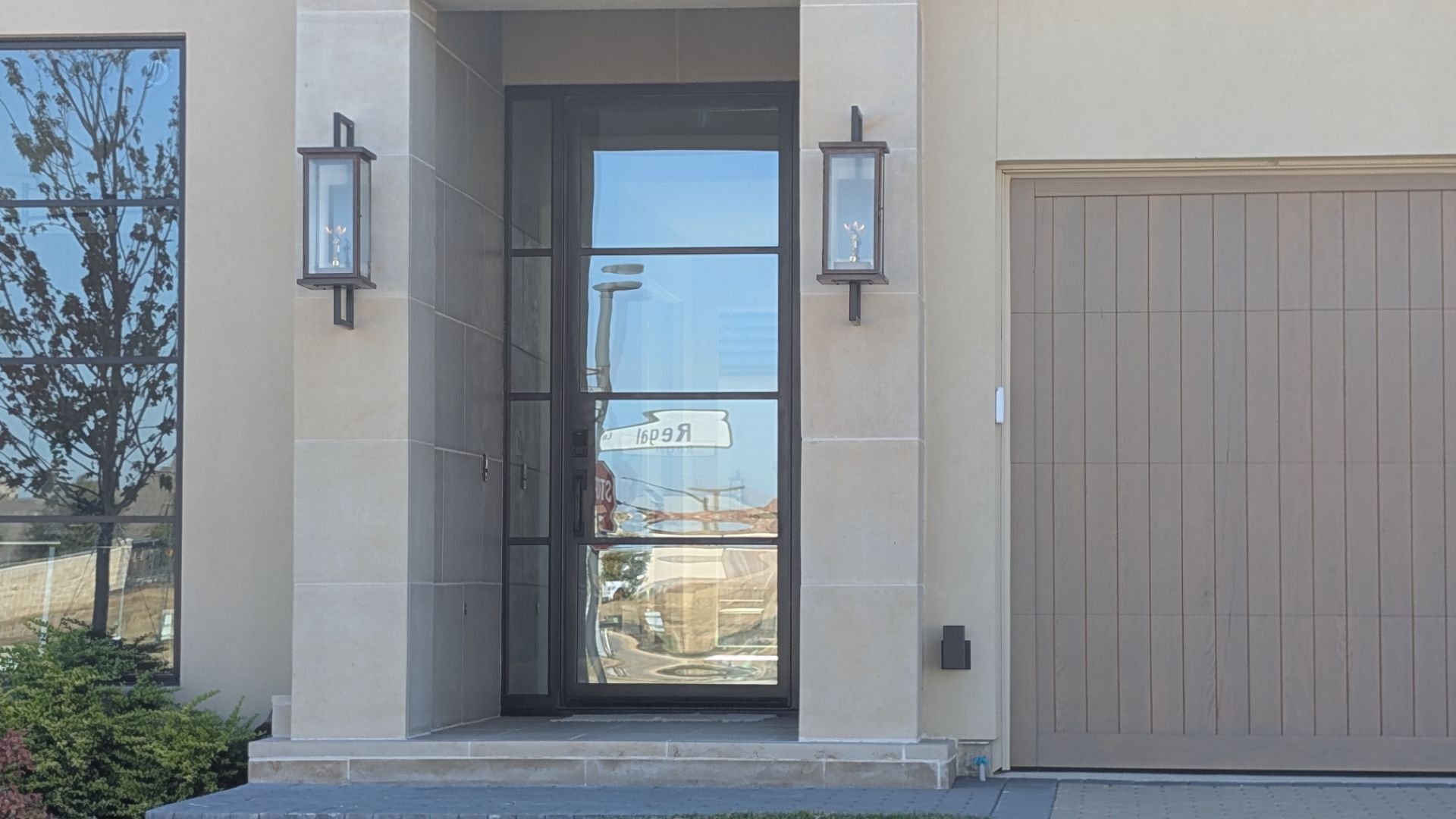 Exterior view of a modern home's front door with sidelight windows, matching garage door, and sconce lighting.