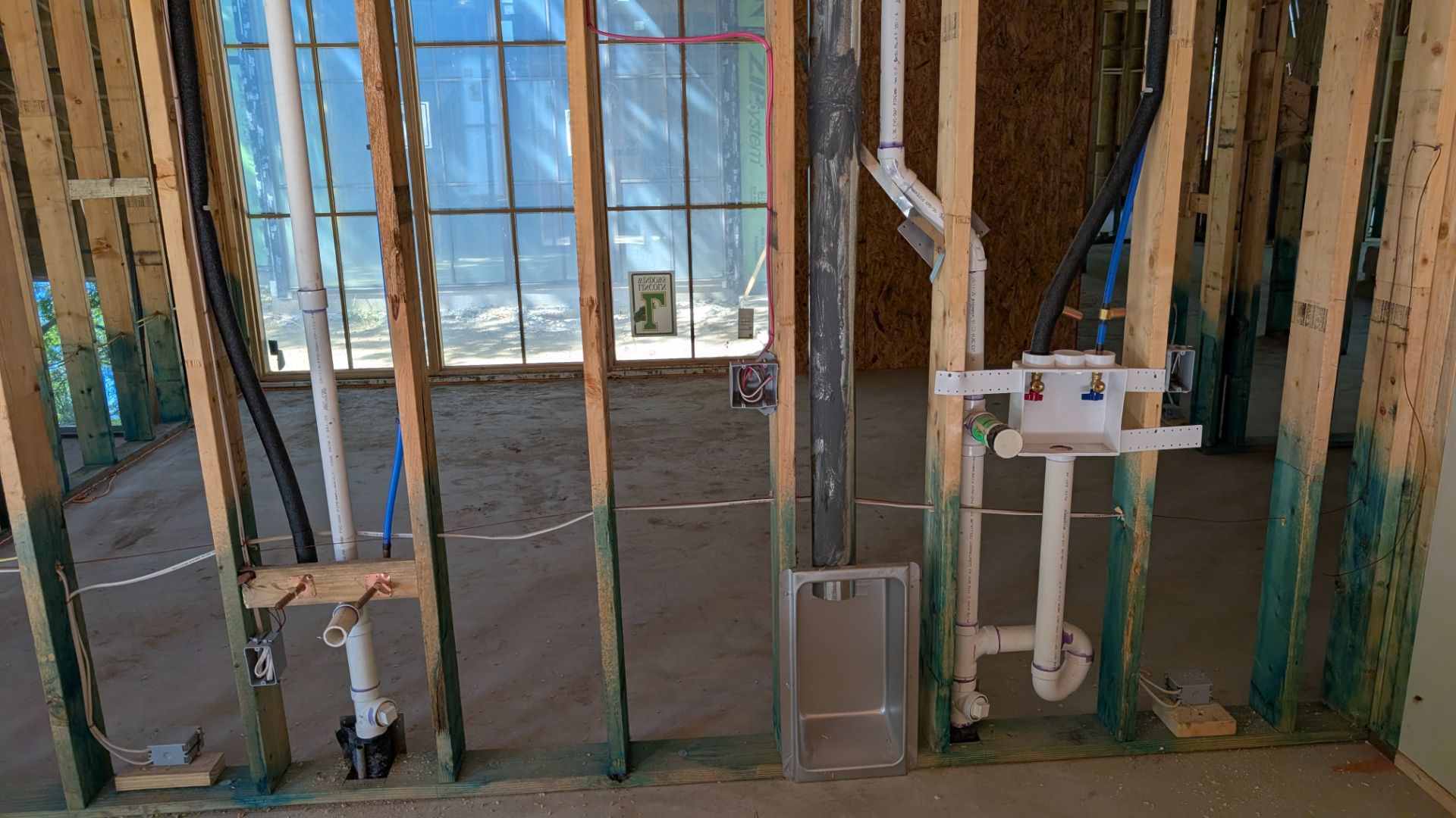 Interior view of unfinished construction; exposed wooden framing with plumbing and electrical fixtures visible.