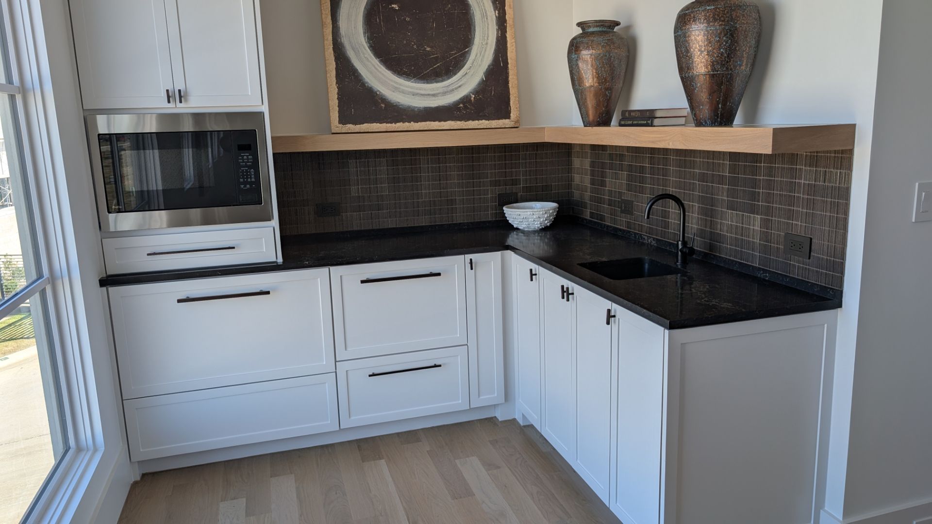 White kitchenette with black countertops, microwave, sink, and decorative items.