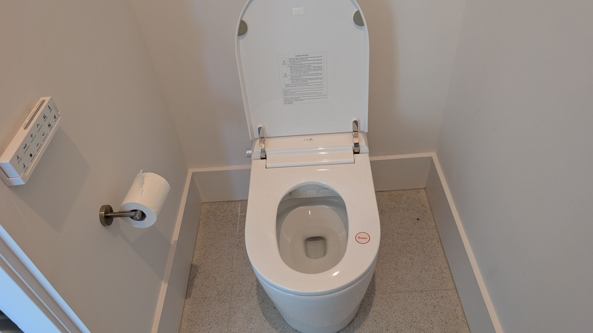 White toilet with the lid up in a small bathroom. Toilet paper roll mounted on the wall.