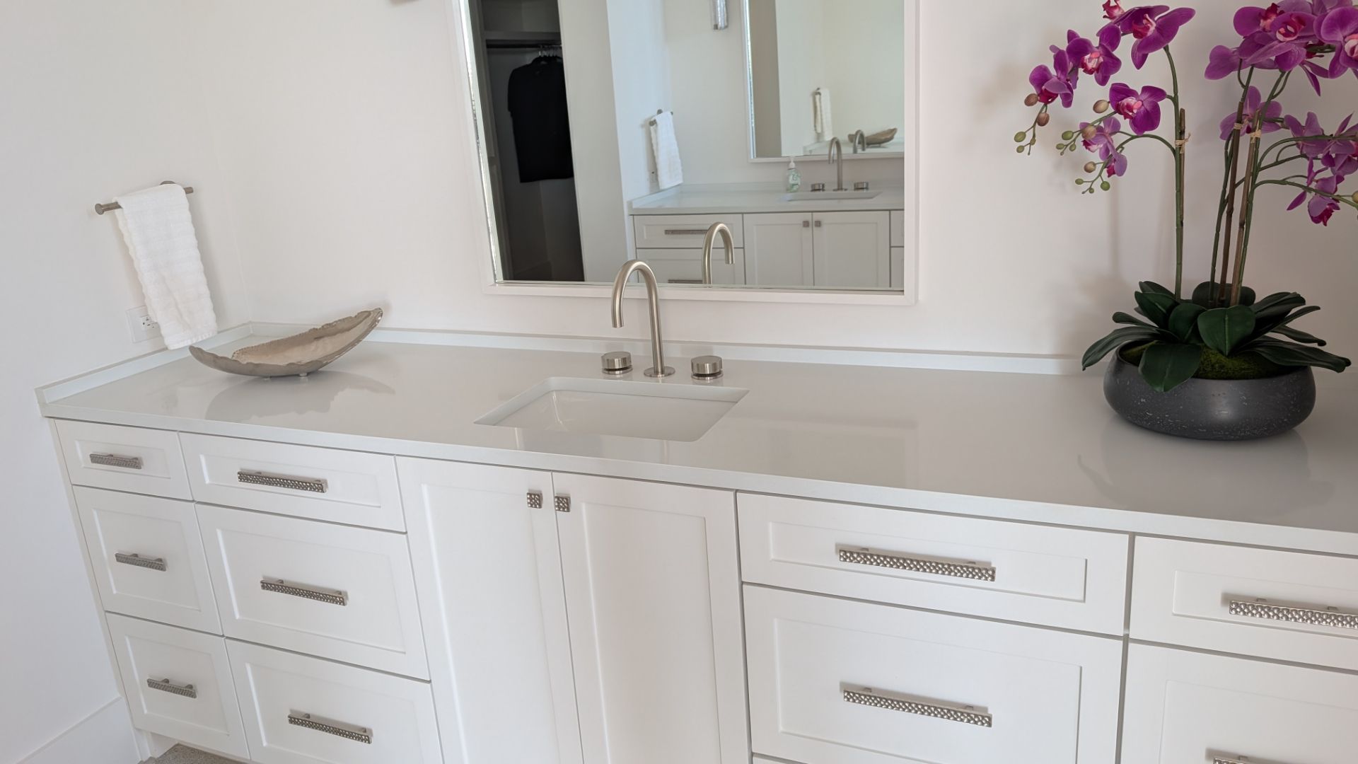 White bathroom vanity with sink, mirror, and orchid plant.