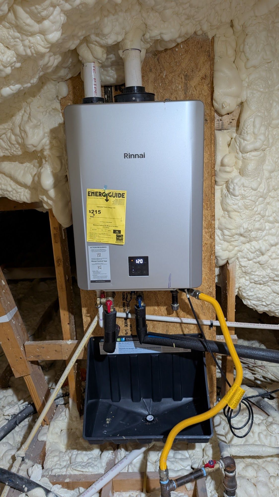 Tankless water heater installed in an attic with insulated foam walls. Yellow gas line visible.