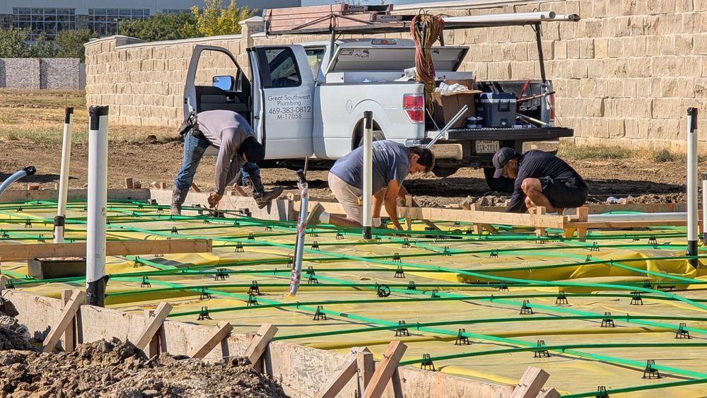 Construction workers installing a concrete foundation. A truck is parked nearby.
