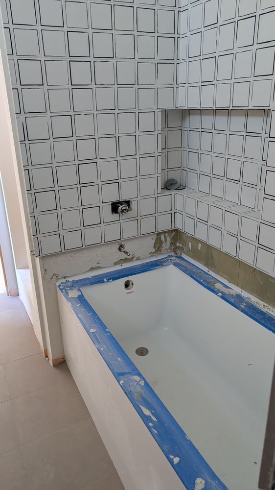 Bathroom renovation in progress: white bathtub, tiled shower wall with alcove, and open doorway.