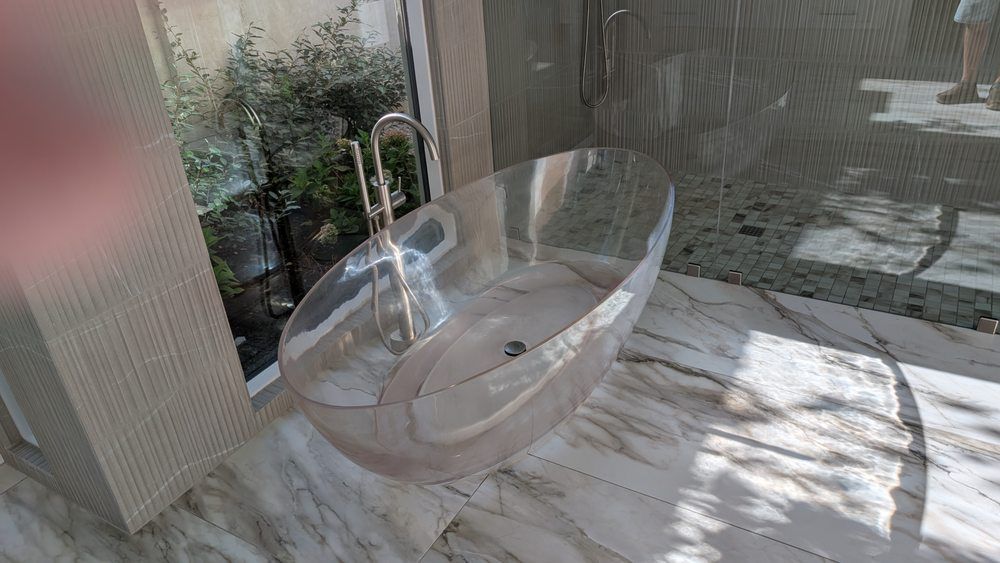Modern stainless steel soaking tub near a window, marble floor, and shower.