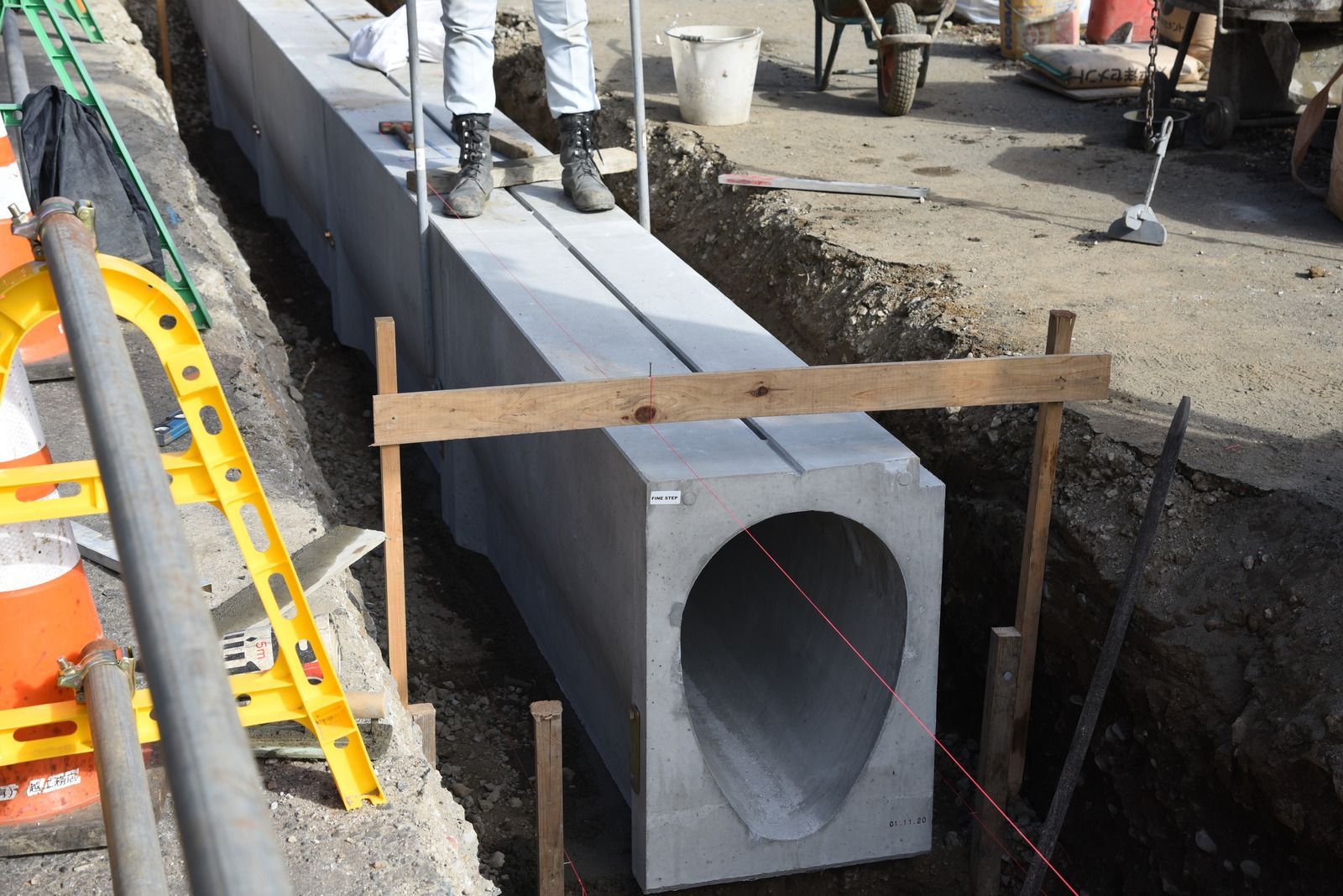 Workers installing a large concrete culvert in a trench at a construction site.