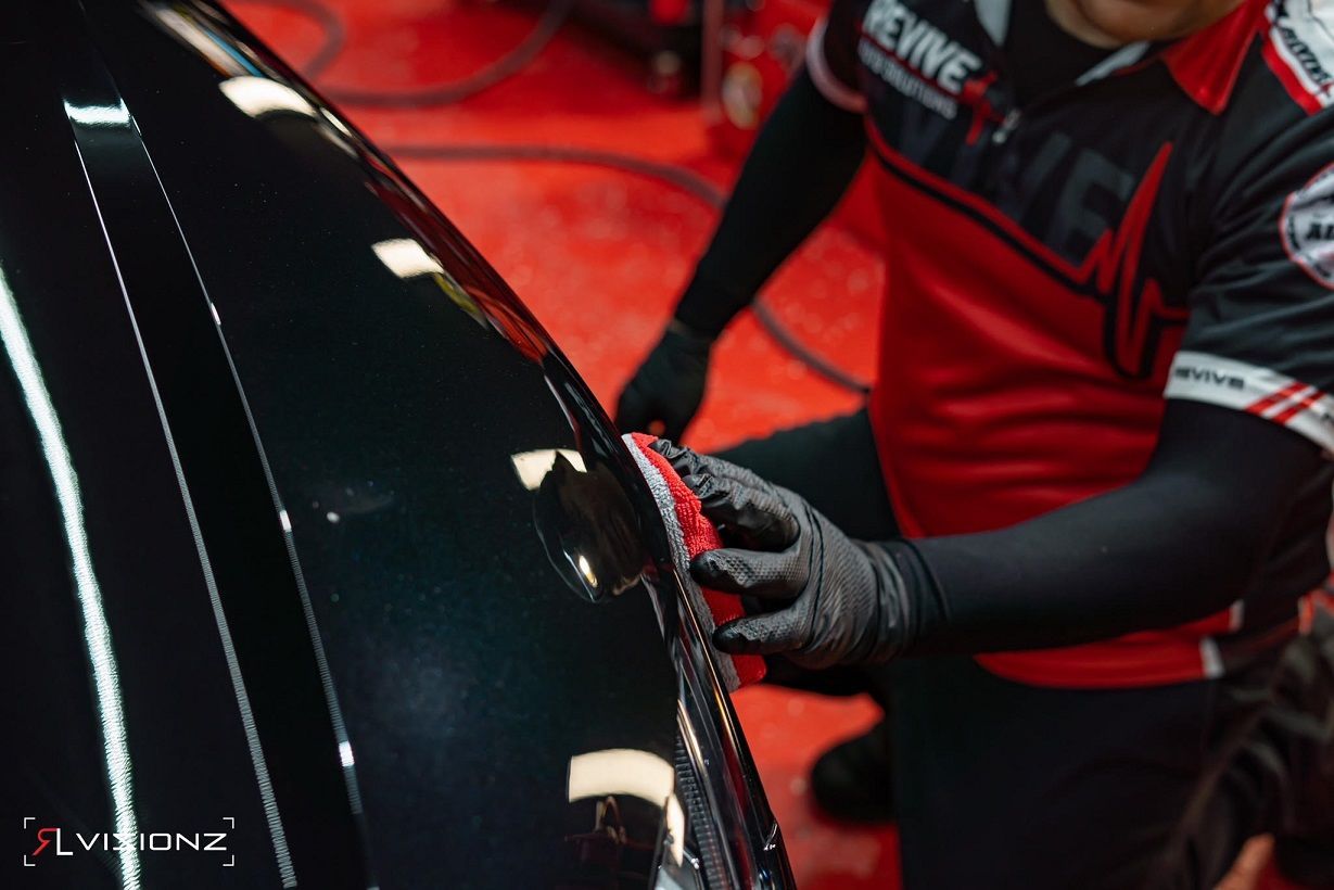 Person in black gloves applies a product to a black car surface with a red applicator.