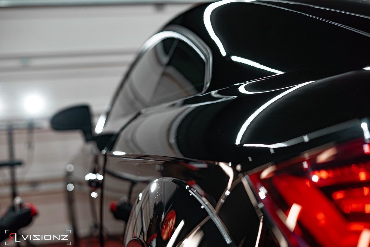 Black car with glossy finish, reflecting bright overhead lights. Red taillight visible.