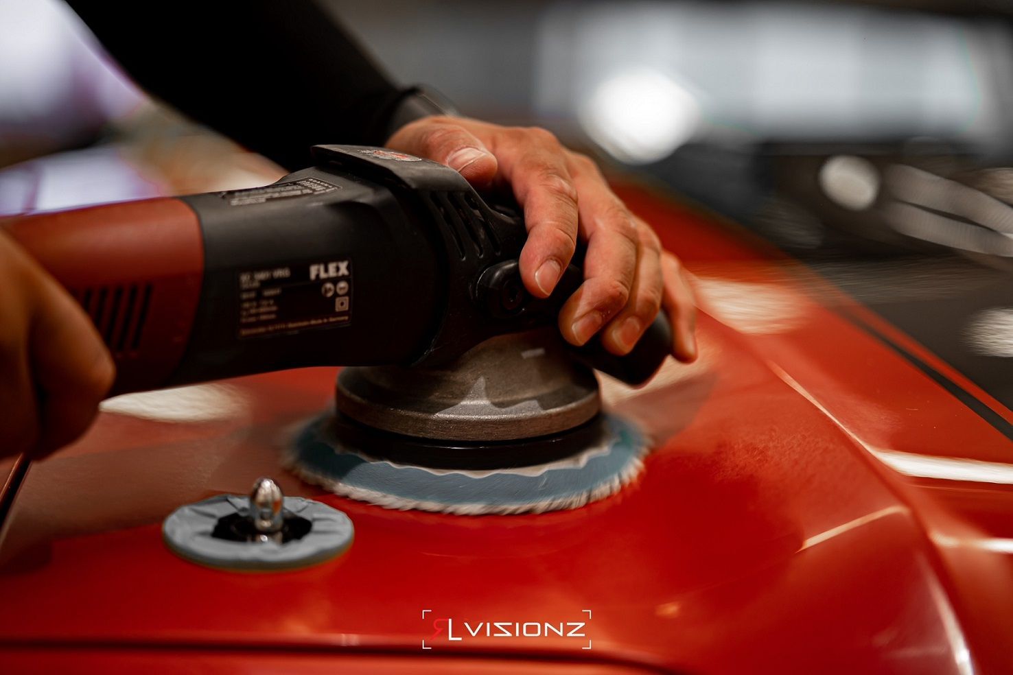 Person polishes a red car with a power buffer.