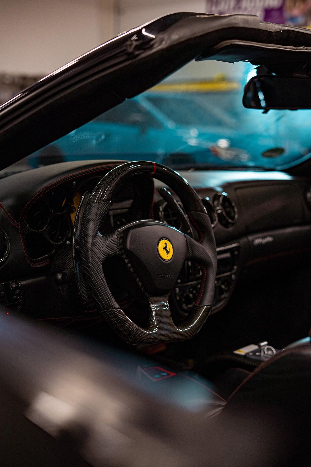 Black Ferrari convertible interior, carbon fiber steering wheel with yellow emblem, view from driver's seat.