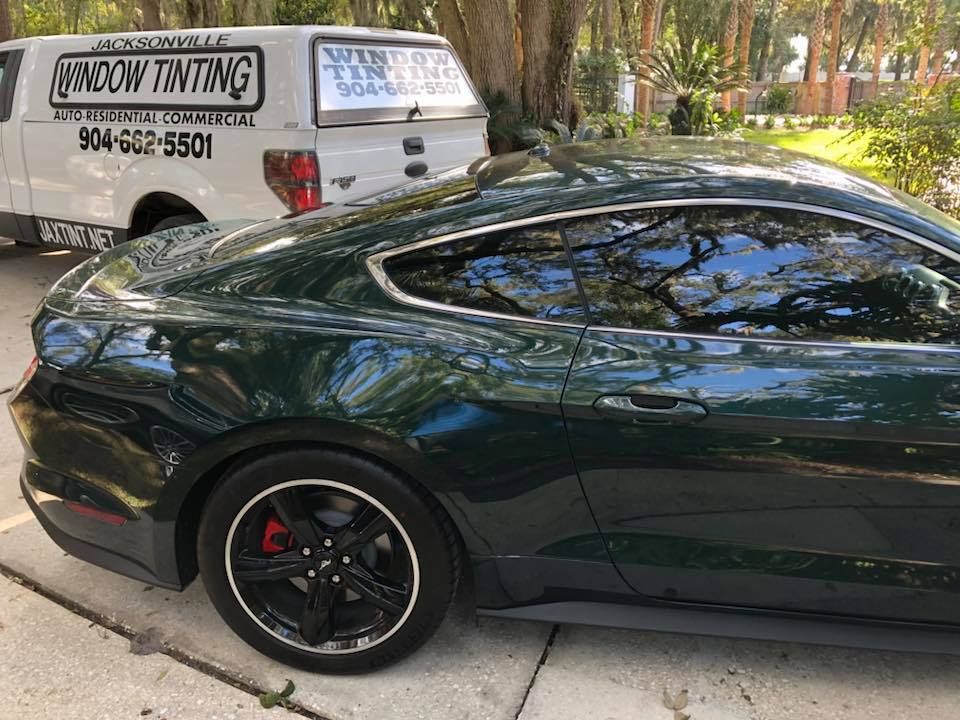 A green mustang is parked in a driveway next to a window tinting van.