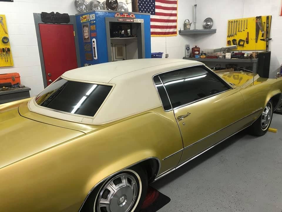 A gold car with a white top is parked in a garage.