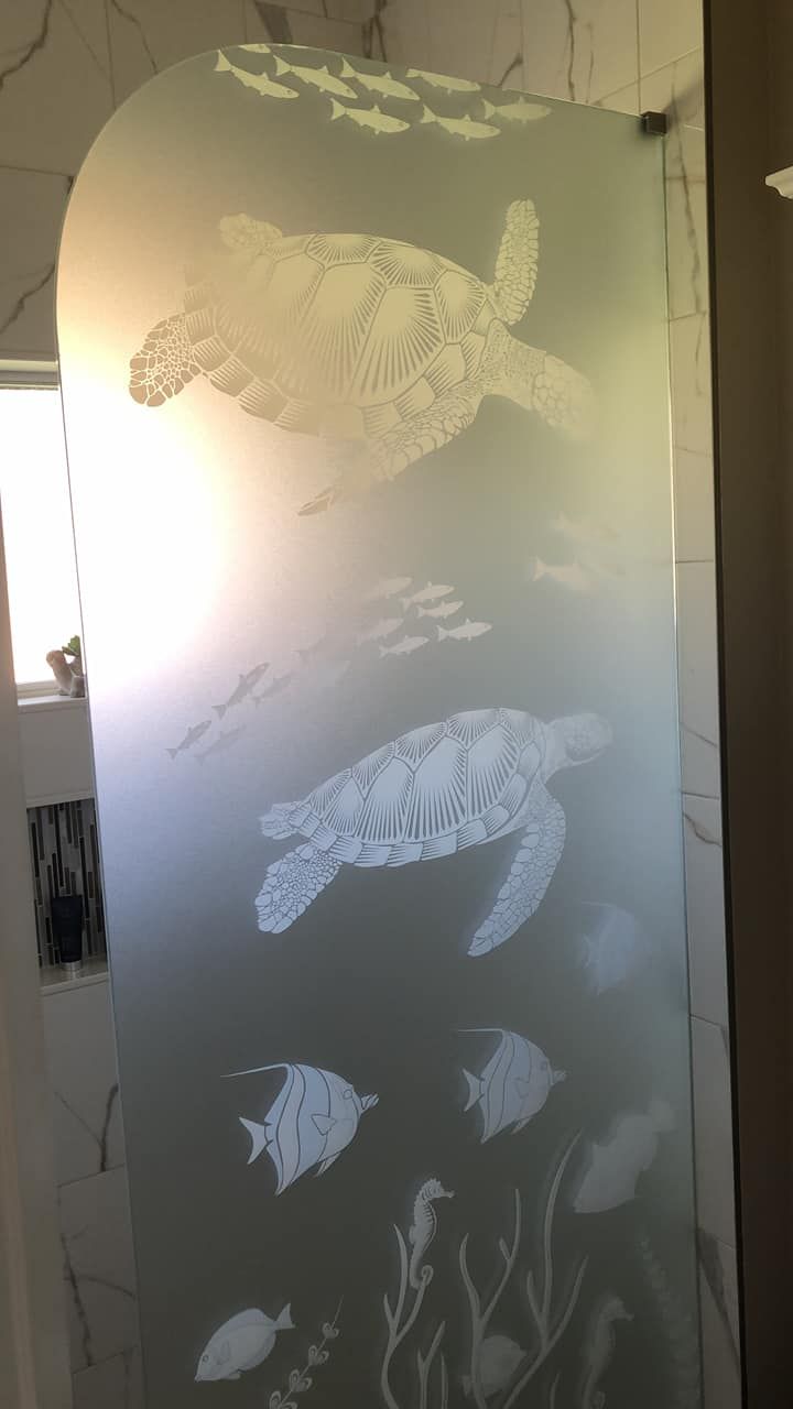 A shower door with a picture of sea turtles and fish on it.
