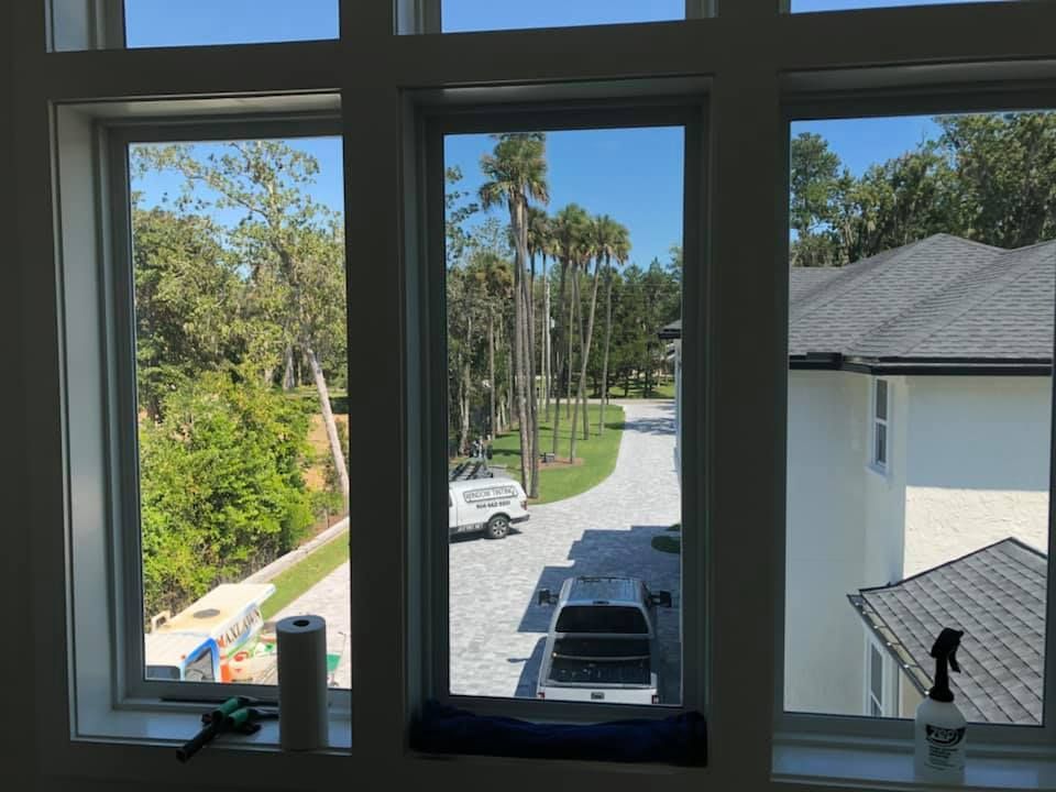 Three windows with a view of a driveway and palm trees