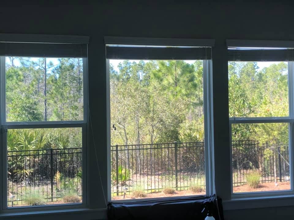 A room with three windows looking out to a fence and trees.