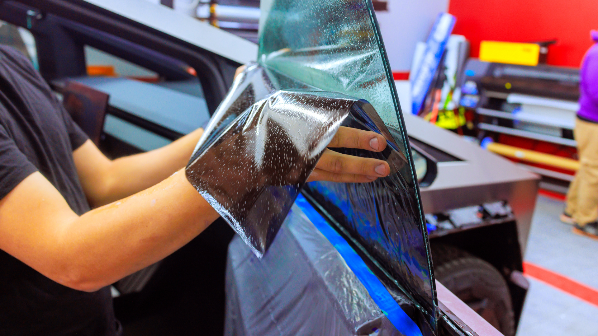 A man is applying tinted glass to a car window.