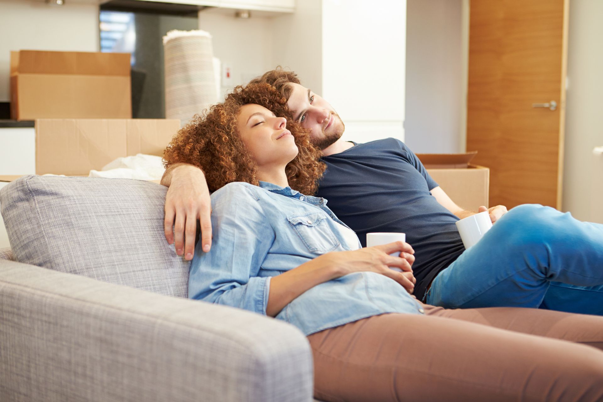 A man and a woman are laying on a couch in a living room.