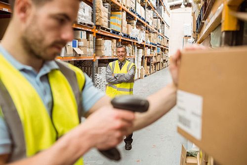 Warehouse worker scanning box with worker in back smiling with crossed arms in warehouse in Melbourne