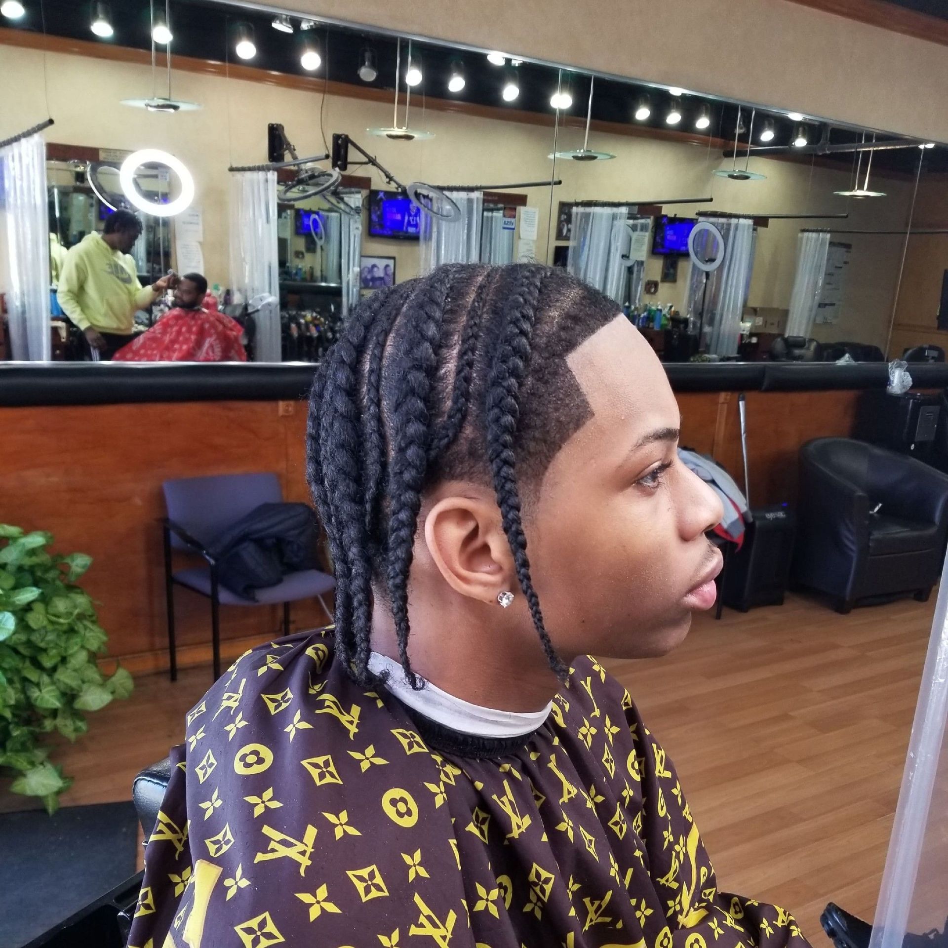 Person with braided hair and fresh haircut in a barber shop wearing a patterned cape.